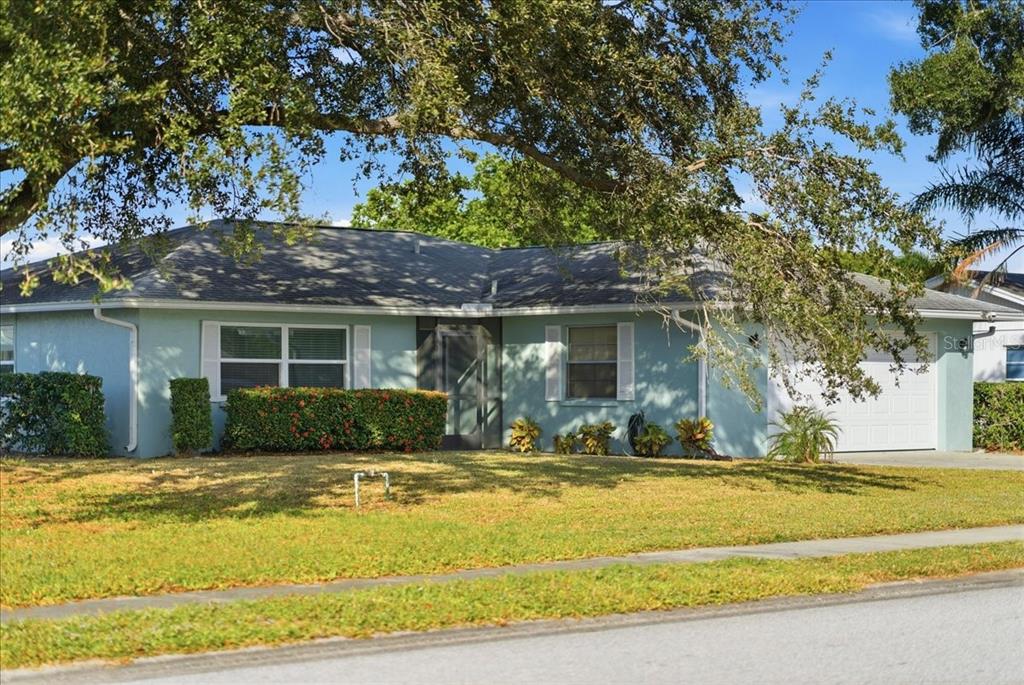 A light blue single-story house with a white garage door and a large front tree — 5883 WHISTLEWOOD CIRCLE, SARASOTA, FL