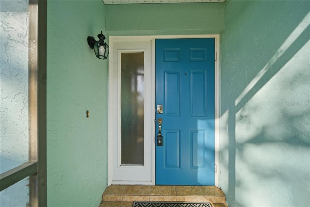 A blue front door with a side window sits on a tiled porch with mint-colored walls — 5883 WHISTLEWOOD CIRCLE, SARASOTA, FL