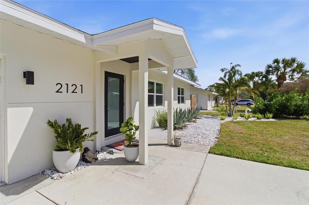 The exterior of a white house features a covered entryway, potted plants, and gravel landscaping — 2121 PALM TERRACE, SARASOTA, FL