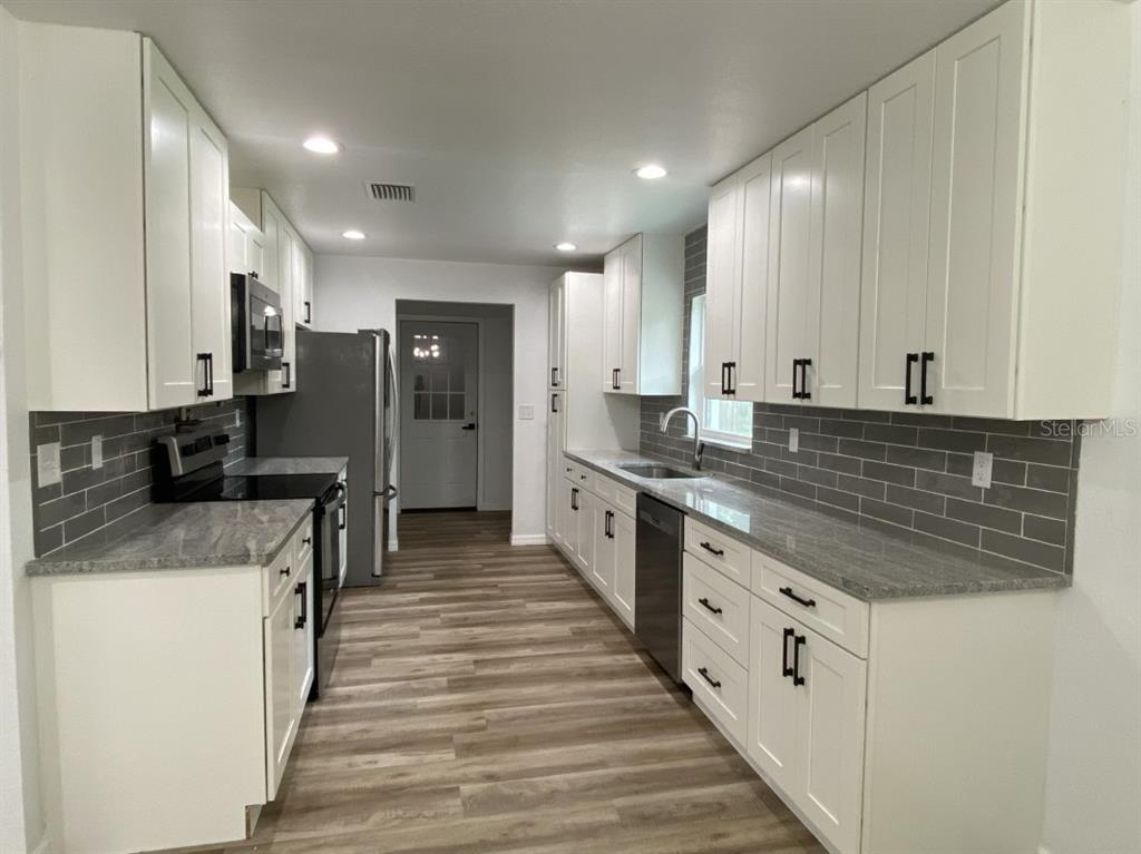 A galley kitchen features white cabinets, gray countertops, a gray subway tile backsplash, and wood-look flooring — 4333 NE 22ND COURT, OCALA, FL