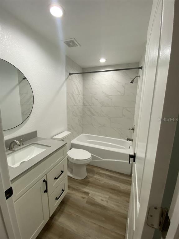A bathroom features a white vanity, a round mirror, a toilet, and a tiled bathtub — 4333 NE 22ND COURT, OCALA, FL