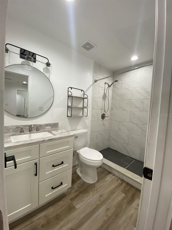 A bathroom features a white vanity, a round mirror, a toilet, and a tiled walk-in shower — 4333 NE 22ND COURT, OCALA, FL
