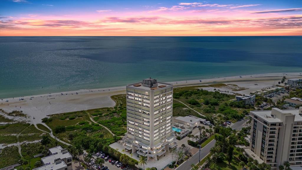 An aerial view shows two high-rise apartment buildings with swimming pools near a coastal town — 5400 OCEAN BOULEVARD UNIT 17-04, SARASOTA, FL