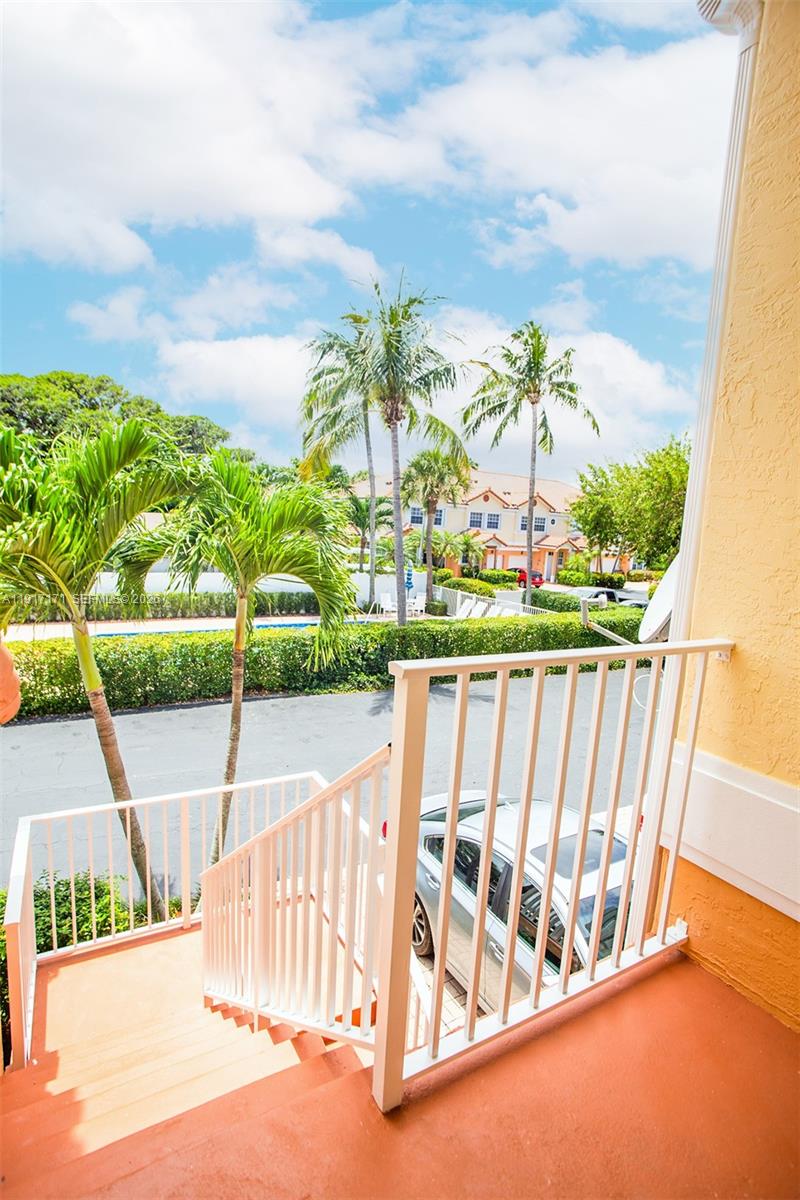 An outdoor balcony with white railings overlooks a parking area, palm trees, and residential buildings — 1998 NE 7th St # 104, Deerfield Beach FL 33441, DEERFIELD BEACH, FL