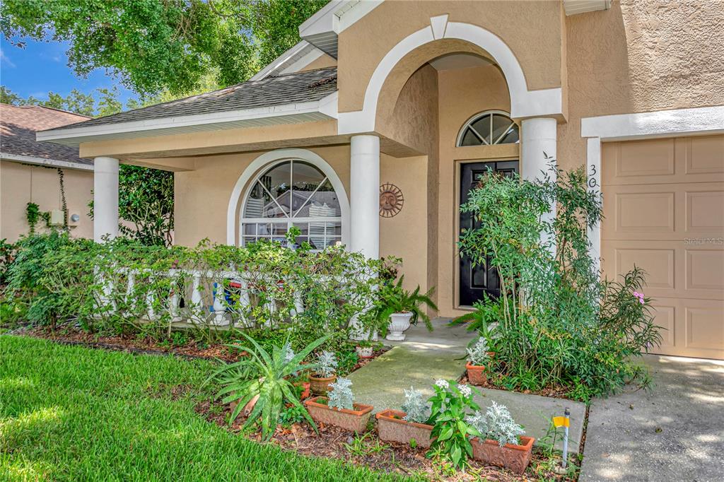 A tan house exterior features a covered front porch, arched window, and a garage door — 3049 BEAVER POND TRAIL, VALRICO, FL
