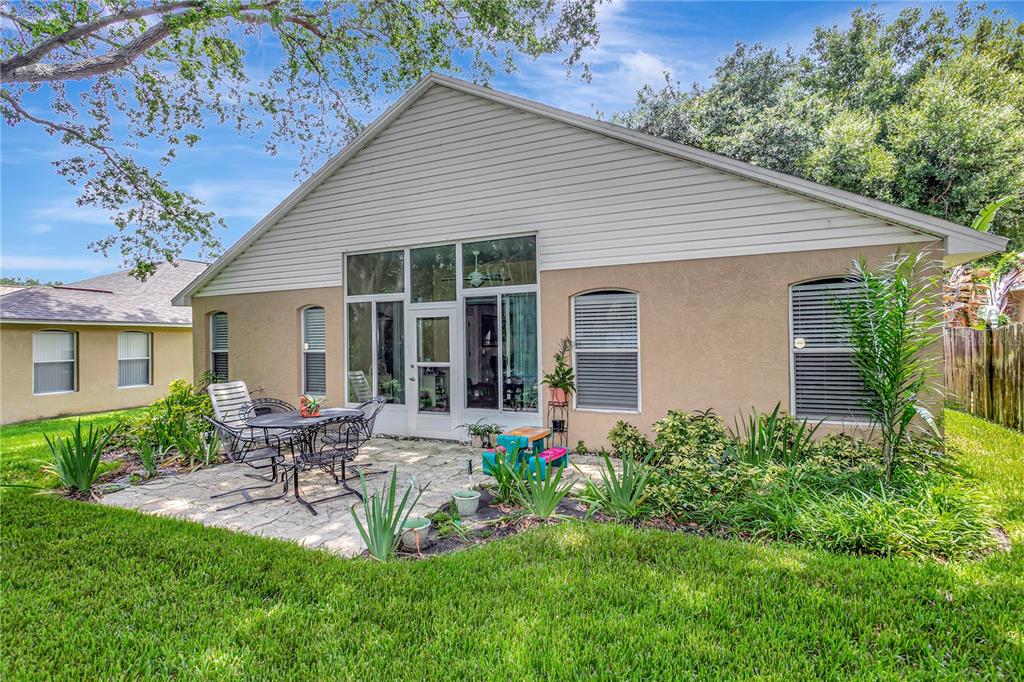 A backyard view of a house featuring a stone patio, screened-in porch, and grassy lawn — 3049 BEAVER POND TRAIL, VALRICO, FL