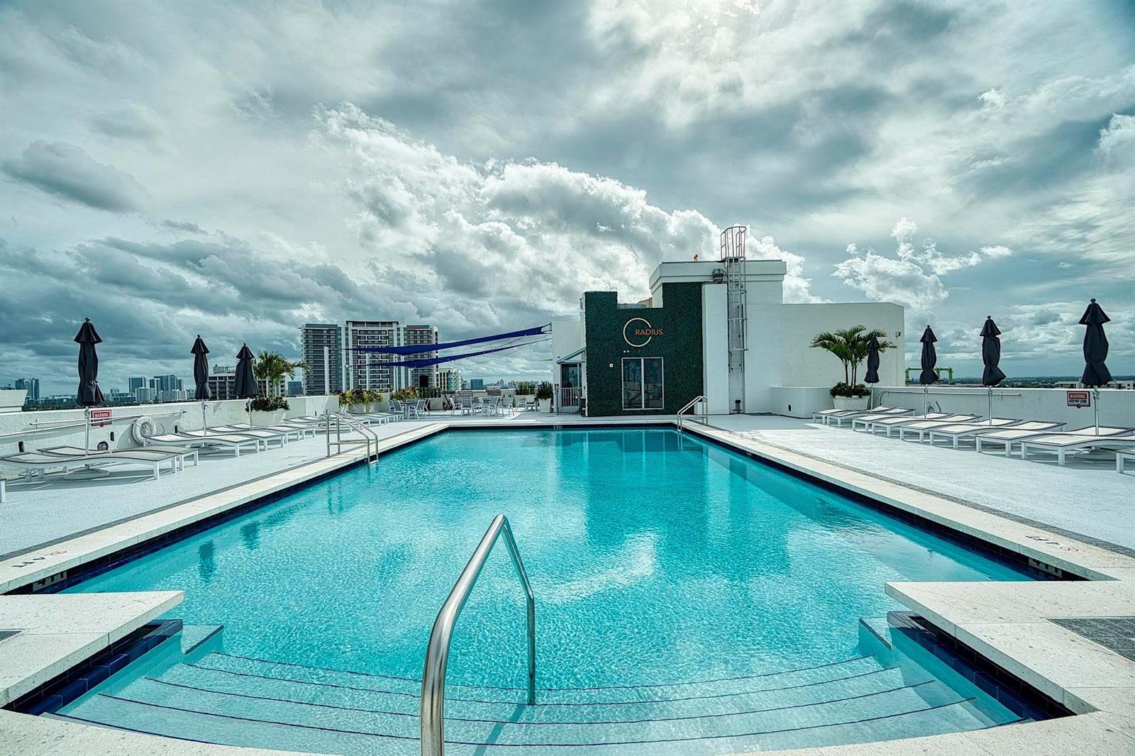 A rooftop swimming pool with lounge chairs and umbrellas under a cloudy sky — 1830 Radius Drive # 912, Hollywood FL 33020, HOLLYWOOD, FL