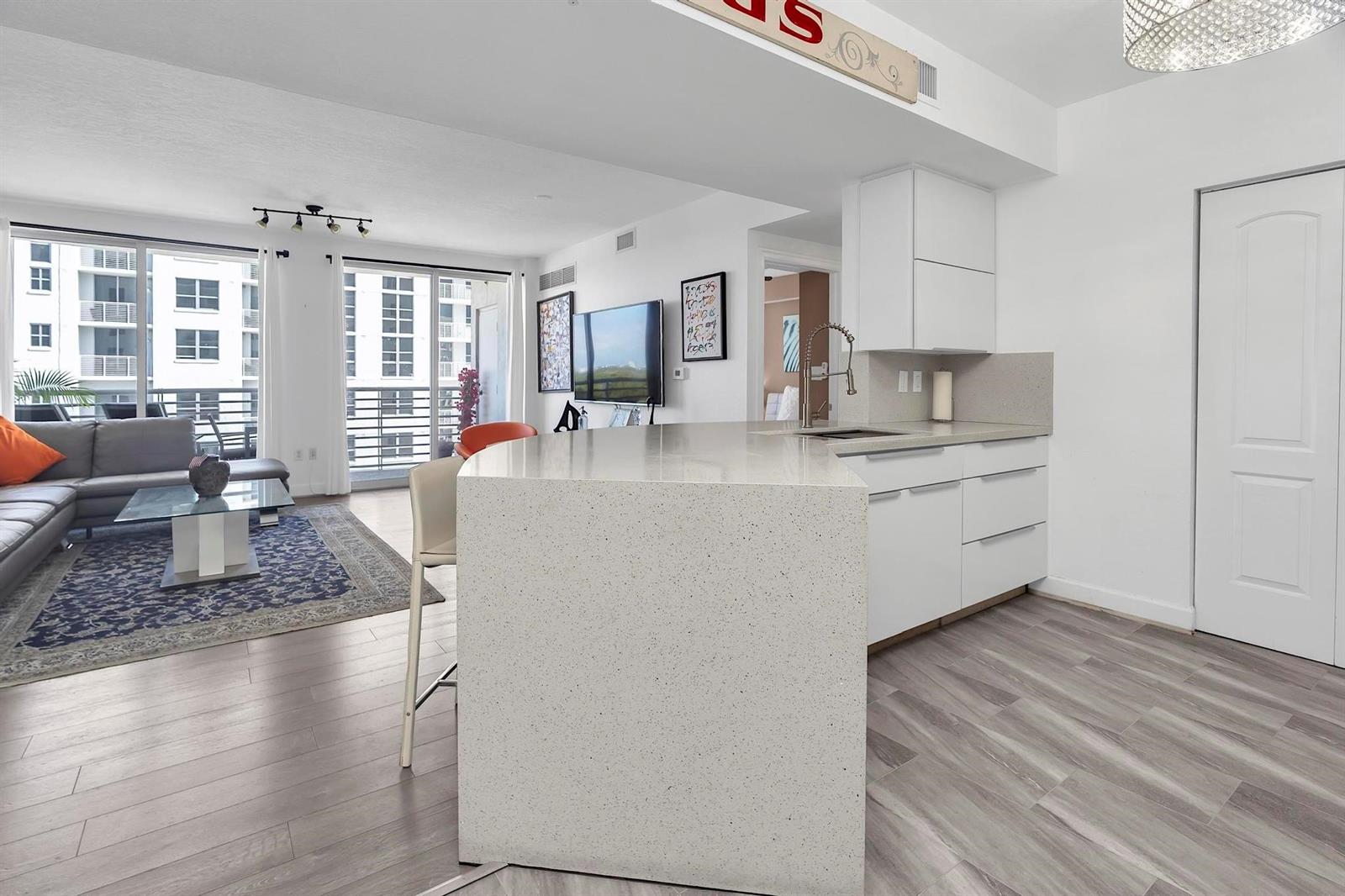 A modern kitchen with a large quartz island overlooks a living room with balcony access — 1830 Radius Drive # 912, Hollywood FL 33020, HOLLYWOOD, FL