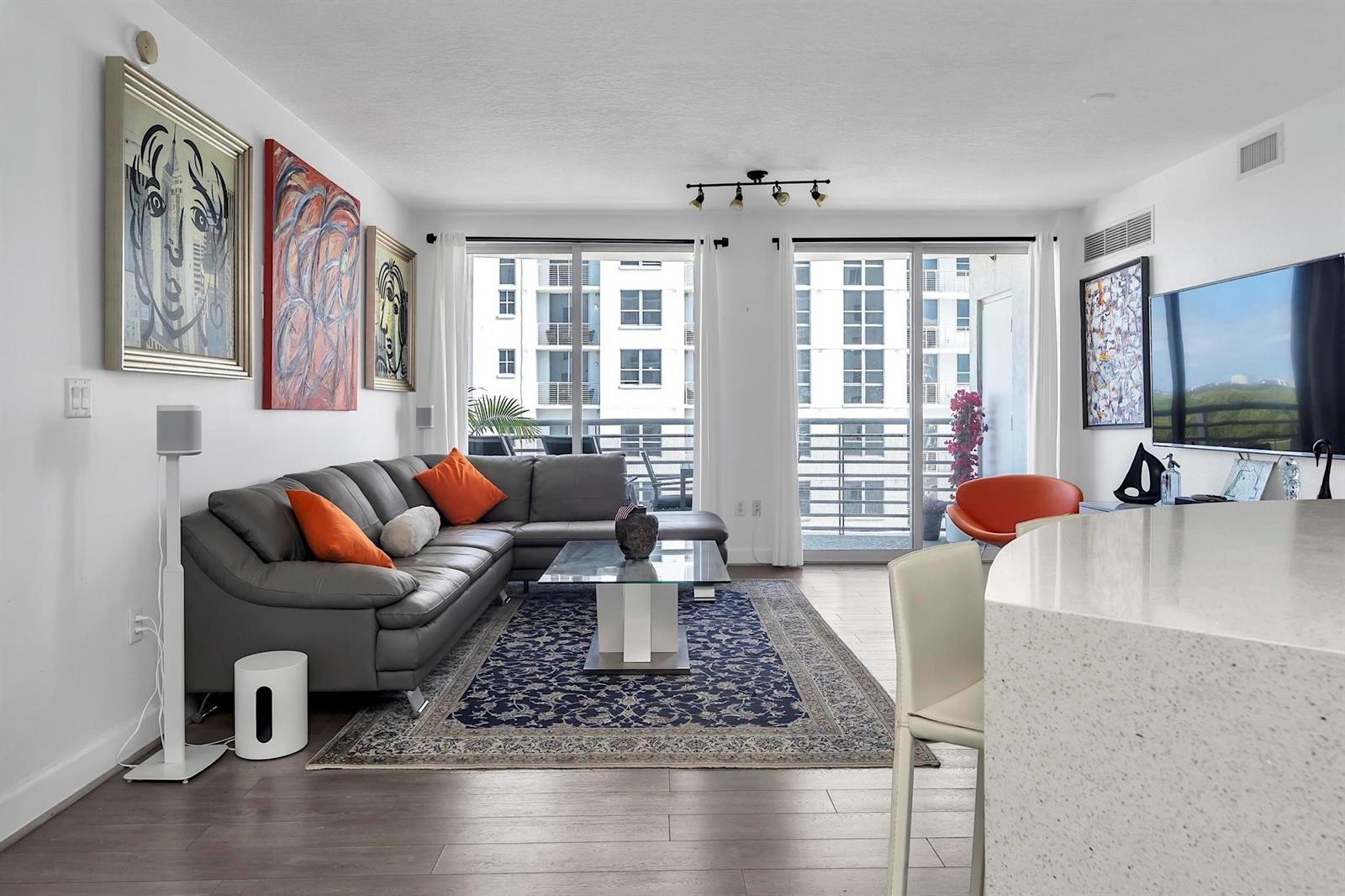 A modern living room features a grey sectional sofa, a patterned rug, and balcony access — 1830 Radius Drive # 912, Hollywood FL 33020, HOLLYWOOD, FL