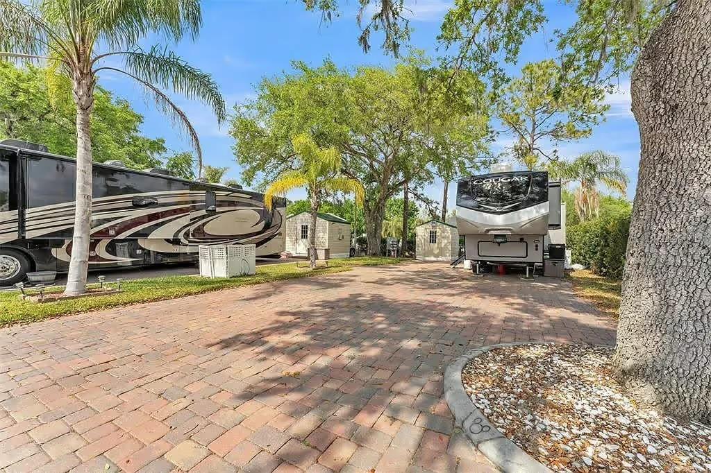 A paved driveway features two parked recreational vehicles and two small sheds under mature trees — 16329 CHERRY TREE COURT, CLERMONT, FL
