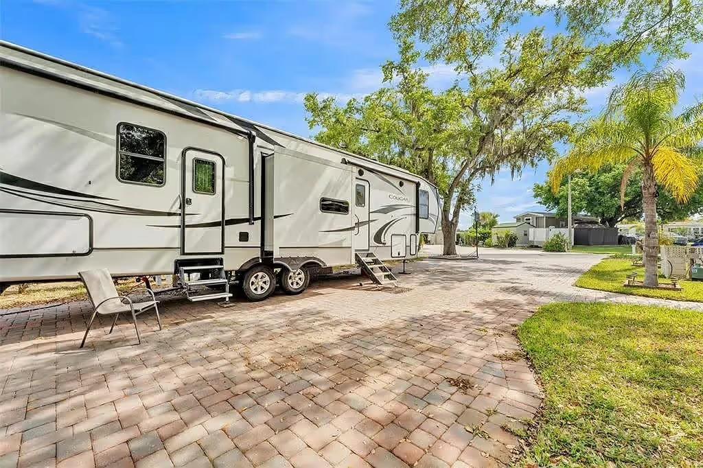 A large white recreational vehicle is parked on a paved brick patio under trees — 16329 CHERRY TREE COURT, CLERMONT, FL