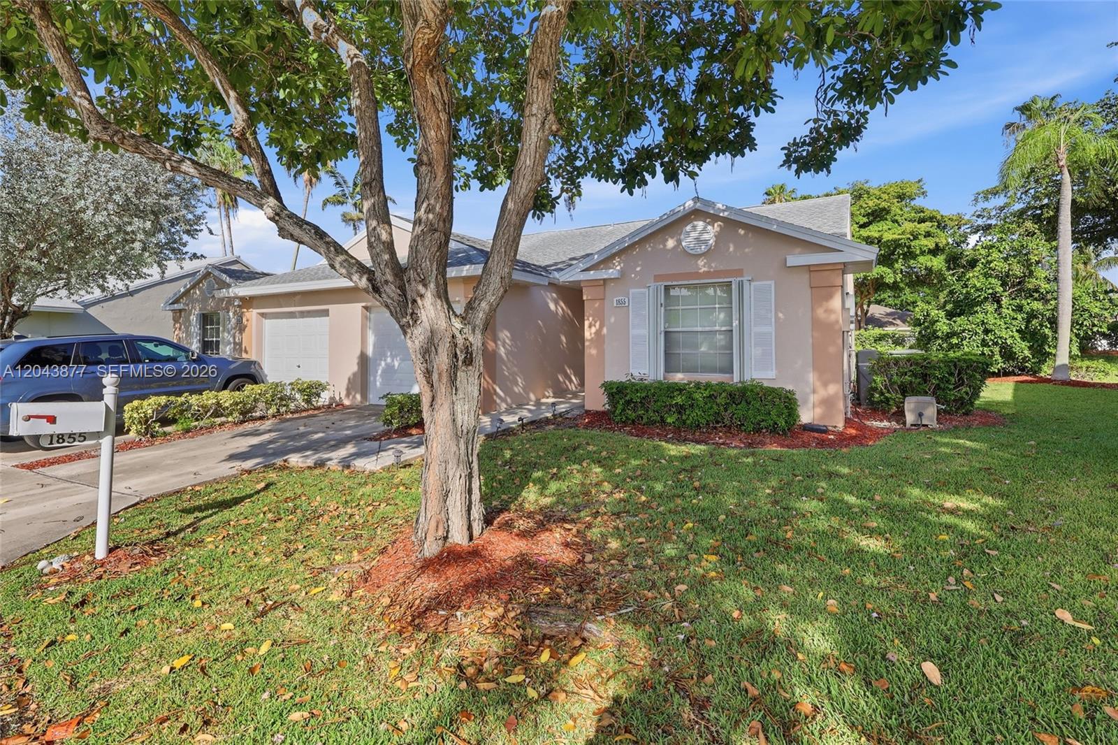 A single-story house with a beige exterior, a two-car garage, and a large front tree — 1855 SE 6th Ct, Homestead FL 33033, HOMESTEAD, FL