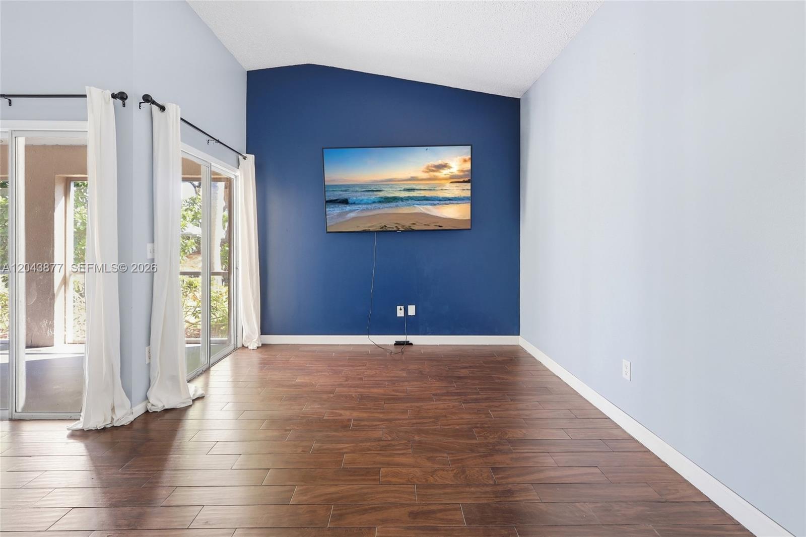 A room with dark wood-look flooring, light blue walls, and a blue accent wall featuring a television — 1855 SE 6th Ct, Homestead FL 33033, HOMESTEAD, FL