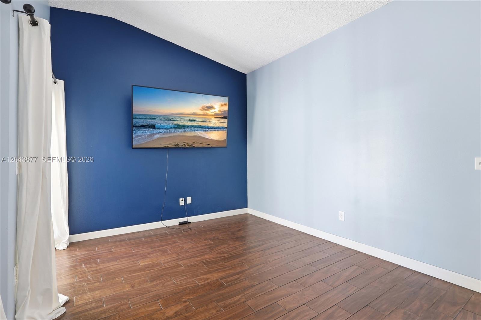 A room features dark wood-look tile flooring, a dark blue accent wall, and a mounted television — 1855 SE 6th Ct, Homestead FL 33033, HOMESTEAD, FL