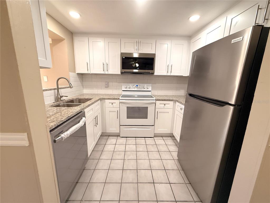 A kitchen features white cabinets, granite countertops, stainless steel appliances, and light-colored floor tiles — 9124 COCHISE LANE, PORT RICHEY, FL