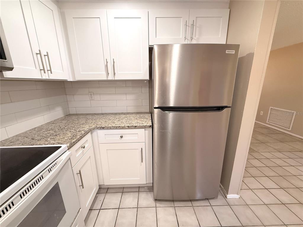 A kitchen features white cabinets, granite countertops, a stainless steel refrigerator, and tiled flooring — 9124 COCHISE LANE, PORT RICHEY, FL