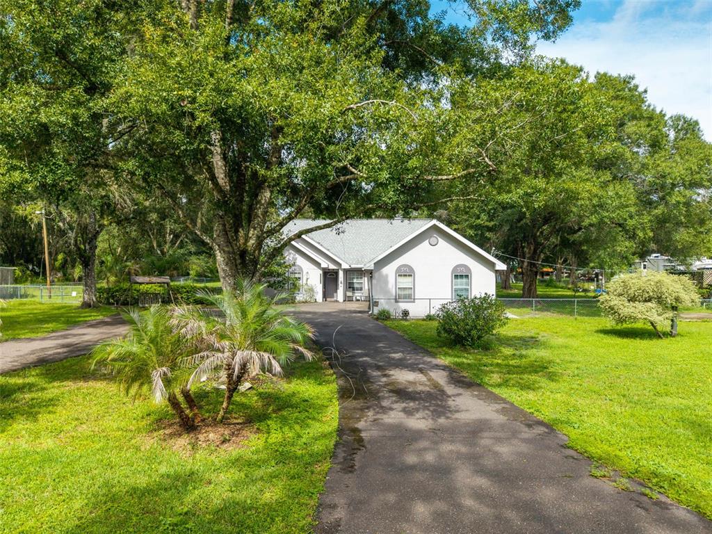 A single-story house with a paved driveway, surrounded by large trees and a grassy lawn — 15370 APACHE DRIVE, THONOTOSASSA, FL