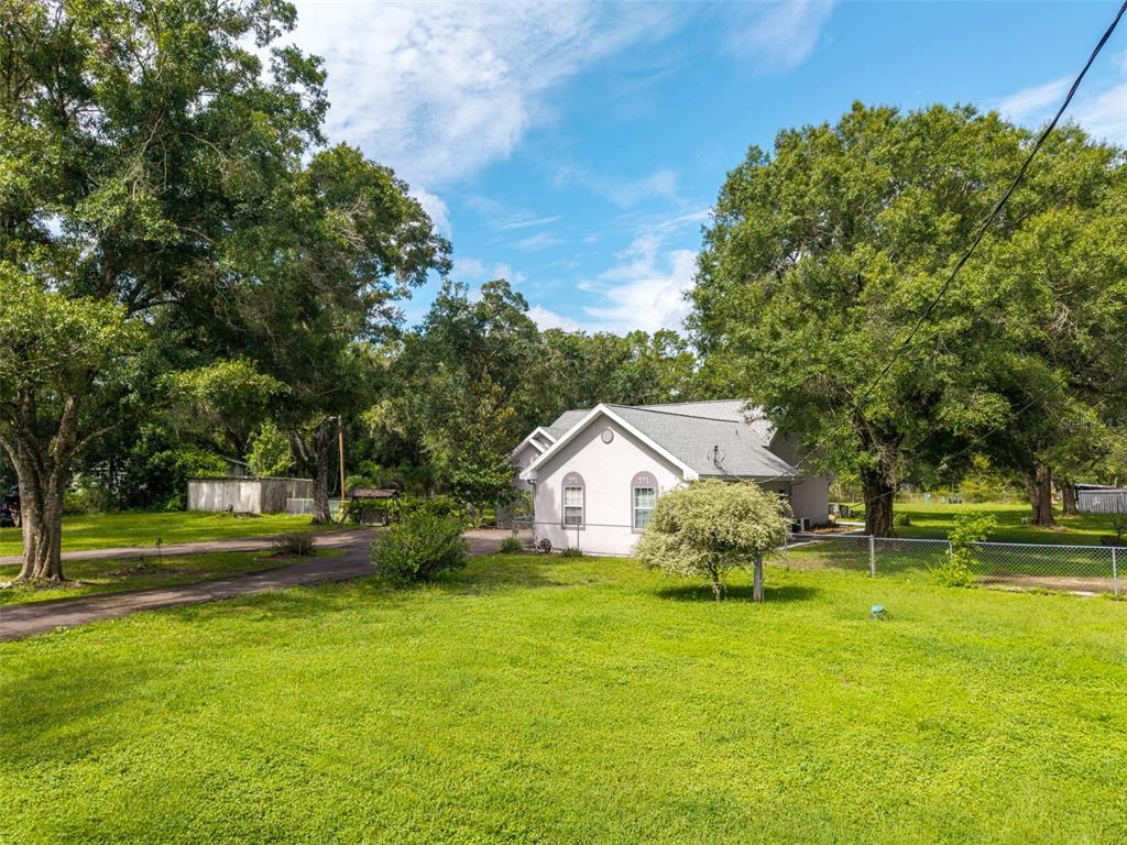 A white house with a gray roof sits on a large, grassy lot with trees — 15370 APACHE DRIVE, THONOTOSASSA, FL