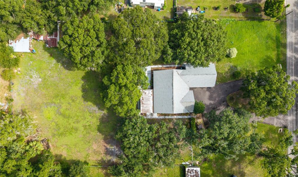 An aerial view shows a house with a gray roof surrounded by trees and grass — 15370 APACHE DRIVE, THONOTOSASSA, FL