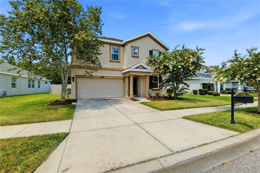 A two-story suburban house with a beige stucco exterior, a two-car garage, and a driveway — 21439 SOUTHERN CHARM DRIVE, LAND O LAKES, FL