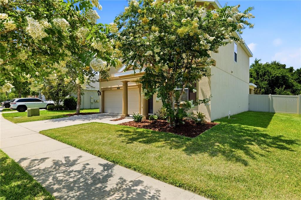 A two-story suburban house with a two-car garage, a front lawn, and flowering trees — 21439 SOUTHERN CHARM DRIVE, LAND O LAKES, FL