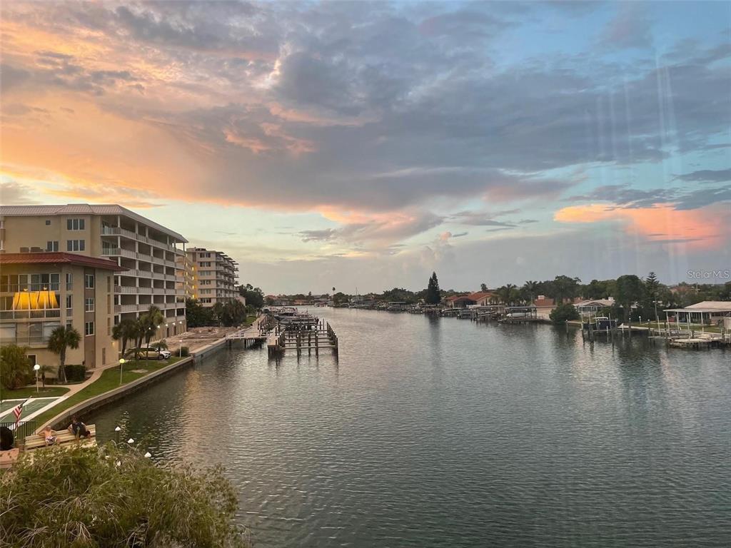 An elevated view of a canal lined with residential buildings, boat docks, and sunset clouds — 105 ISLAND WAY UNIT 138, CLEARWATER BEACH, FL