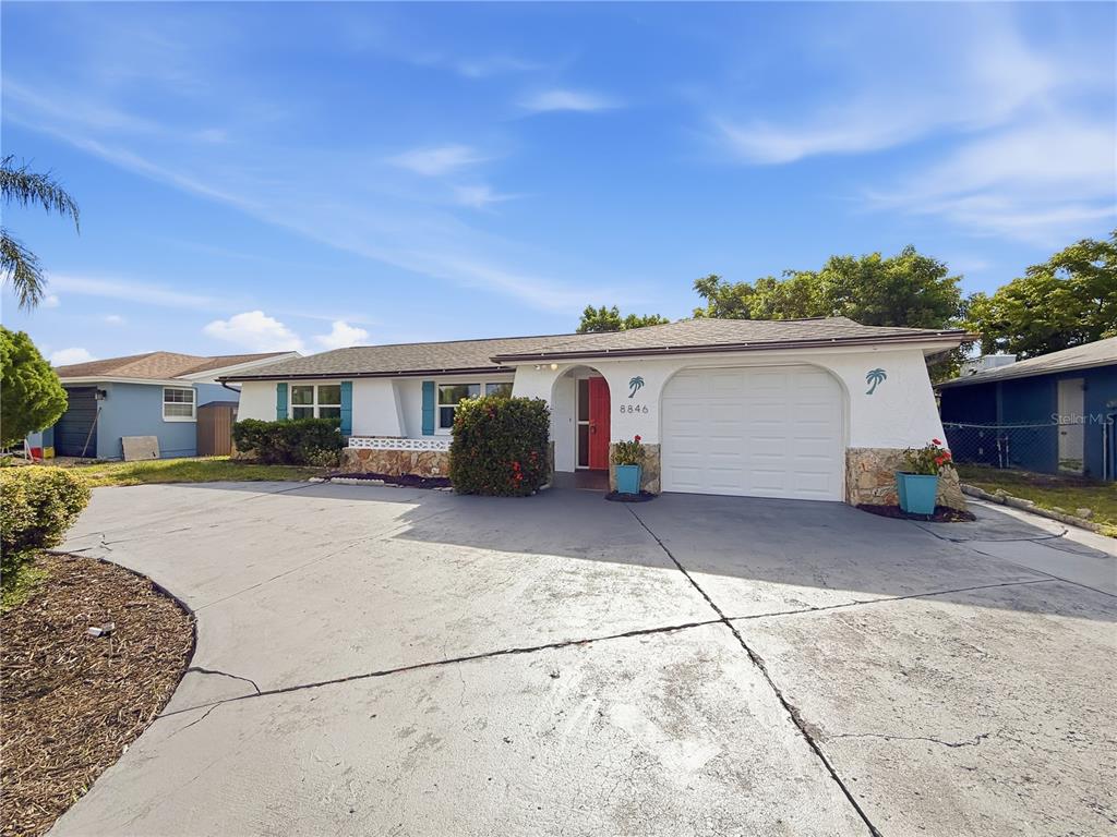 A single-story house with a white stucco exterior, stone accents, and a concrete driveway — 8846 CARMEN LANE, PORT RICHEY, FL
