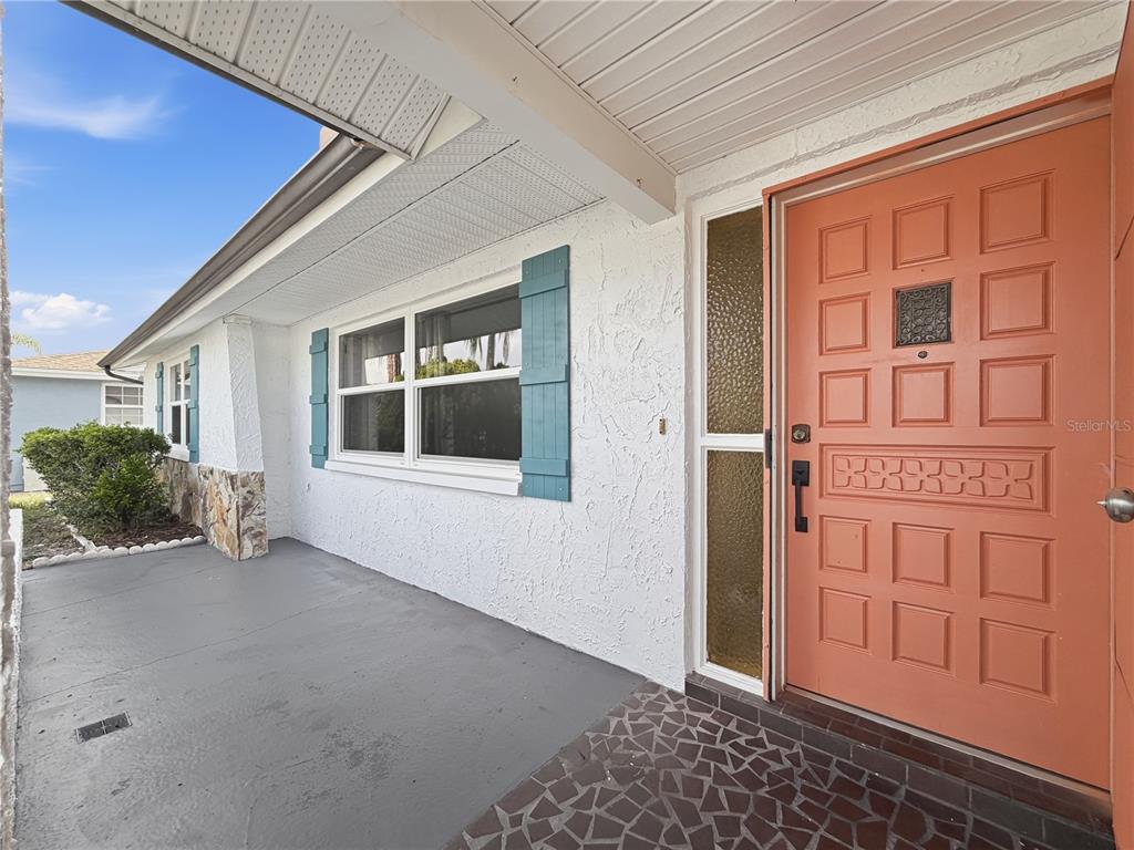 A covered porch features a coral-colored front door, blue shutters, and a stone-accented wall — 8846 CARMEN LANE, PORT RICHEY, FL