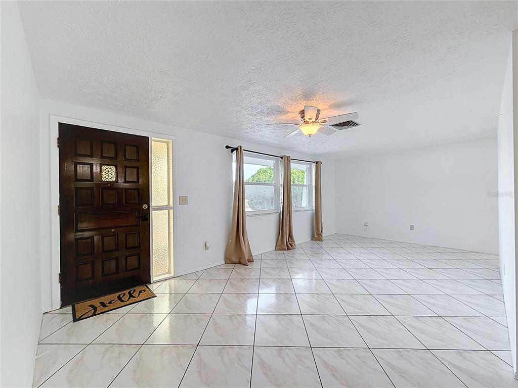 A bright living room features white walls, diagonal marble-patterned tile floors, and a ceiling fan — 8846 CARMEN LANE, PORT RICHEY, FL