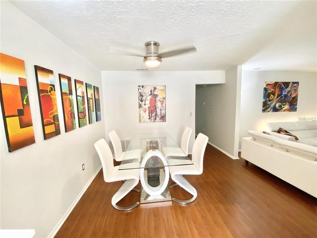 A dining room features a glass table, four white chairs, and artwork on the walls — 225 S TROPICAL TRAIL UNIT 312, MERRITT ISLAND, FL