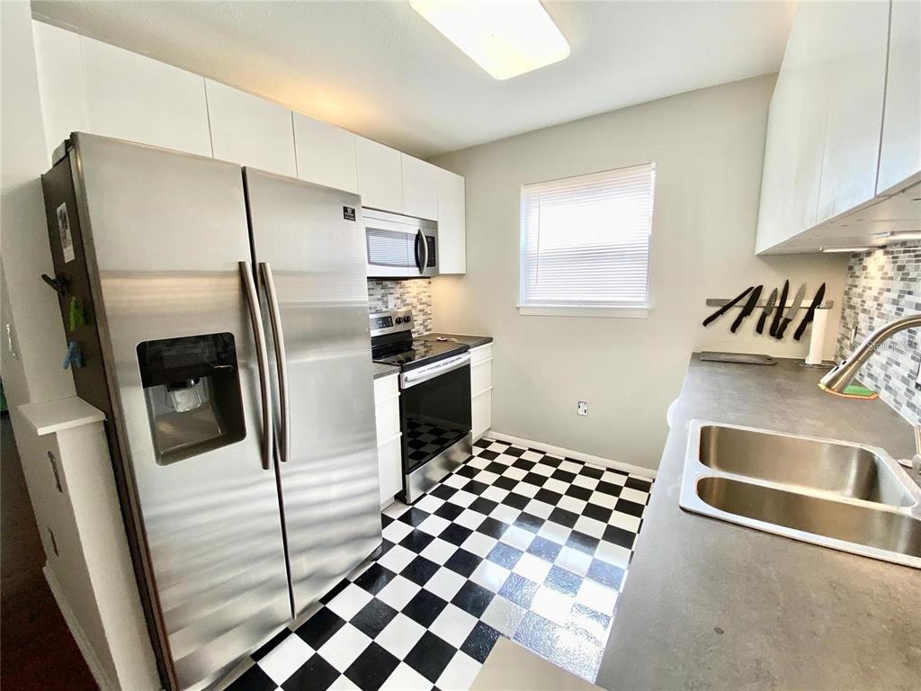 A kitchen features stainless steel appliances, white cabinets, and a black and white checkered floor — 225 S TROPICAL TRAIL UNIT 312, MERRITT ISLAND, FL