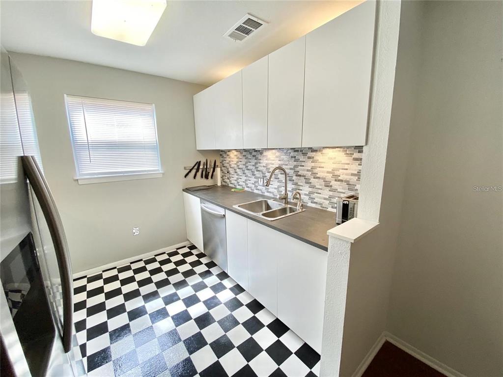 A kitchen features white flat-panel cabinets, a gray countertop, and a black-and-white checkered floor — 225 S TROPICAL TRAIL UNIT 312, MERRITT ISLAND, FL