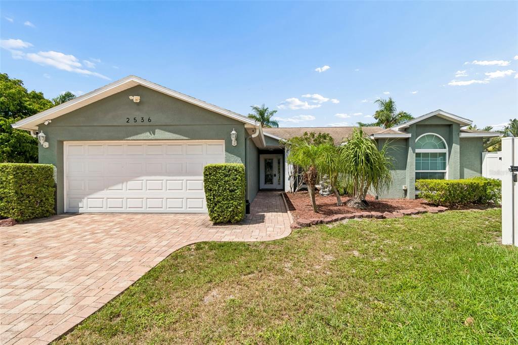 A single-story house with a green exterior, a two-car garage, and a brick paver driveway — 2536 COUNTRYSIDE PINES DRIVE, CLEARWATER, FL