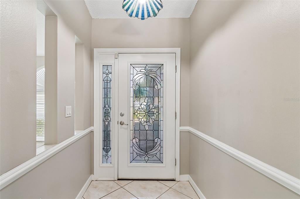 An entryway features a white front door with decorative glass, tile flooring, and beige walls — 2536 COUNTRYSIDE PINES DRIVE, CLEARWATER, FL