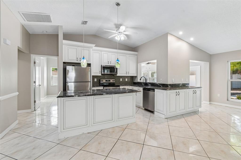 A kitchen features white cabinets, dark countertops, stainless steel appliances, and light-colored tile flooring — 2536 COUNTRYSIDE PINES DRIVE, CLEARWATER, FL
