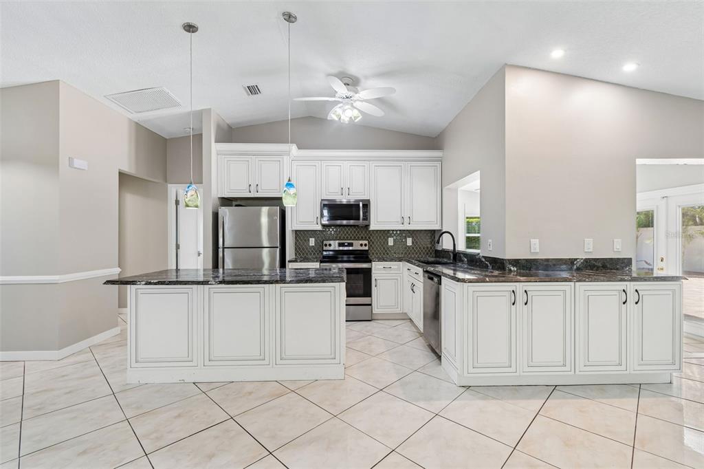 A kitchen with white cabinets, dark countertops, stainless steel appliances, and light-colored tile flooring — 2536 COUNTRYSIDE PINES DRIVE, CLEARWATER, FL