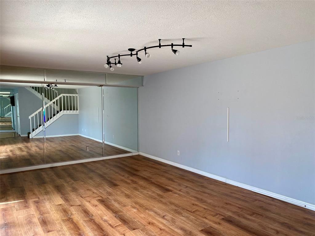 An empty room features wood-look flooring, light gray walls, a mirrored wall, and track lighting — 2942 POPLAR AVENUE, LEESBURG, FL