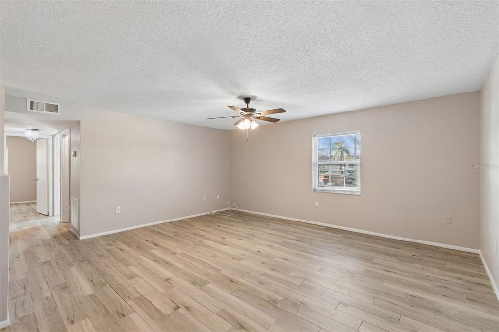 An empty living room features light wood-look flooring, beige walls, and a ceiling fan — 4335 AEGEAN DRIVE UNIT 136A, TAMPA, FL