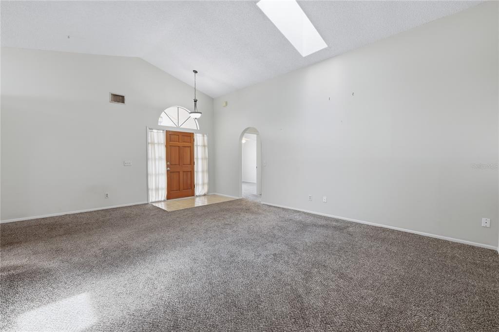 A living and dining area with vaulted ceilings, a skylight, and neutral-toned furniture — 718 BIRGHAM PLACE, LAKE MARY, FL