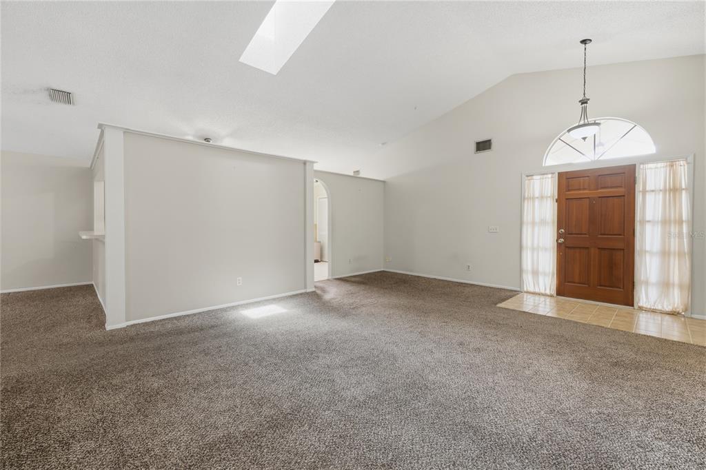 A spacious living room with beige carpet, vaulted ceilings, a skylight, and an arched entryway — 718 BIRGHAM PLACE, LAKE MARY, FL