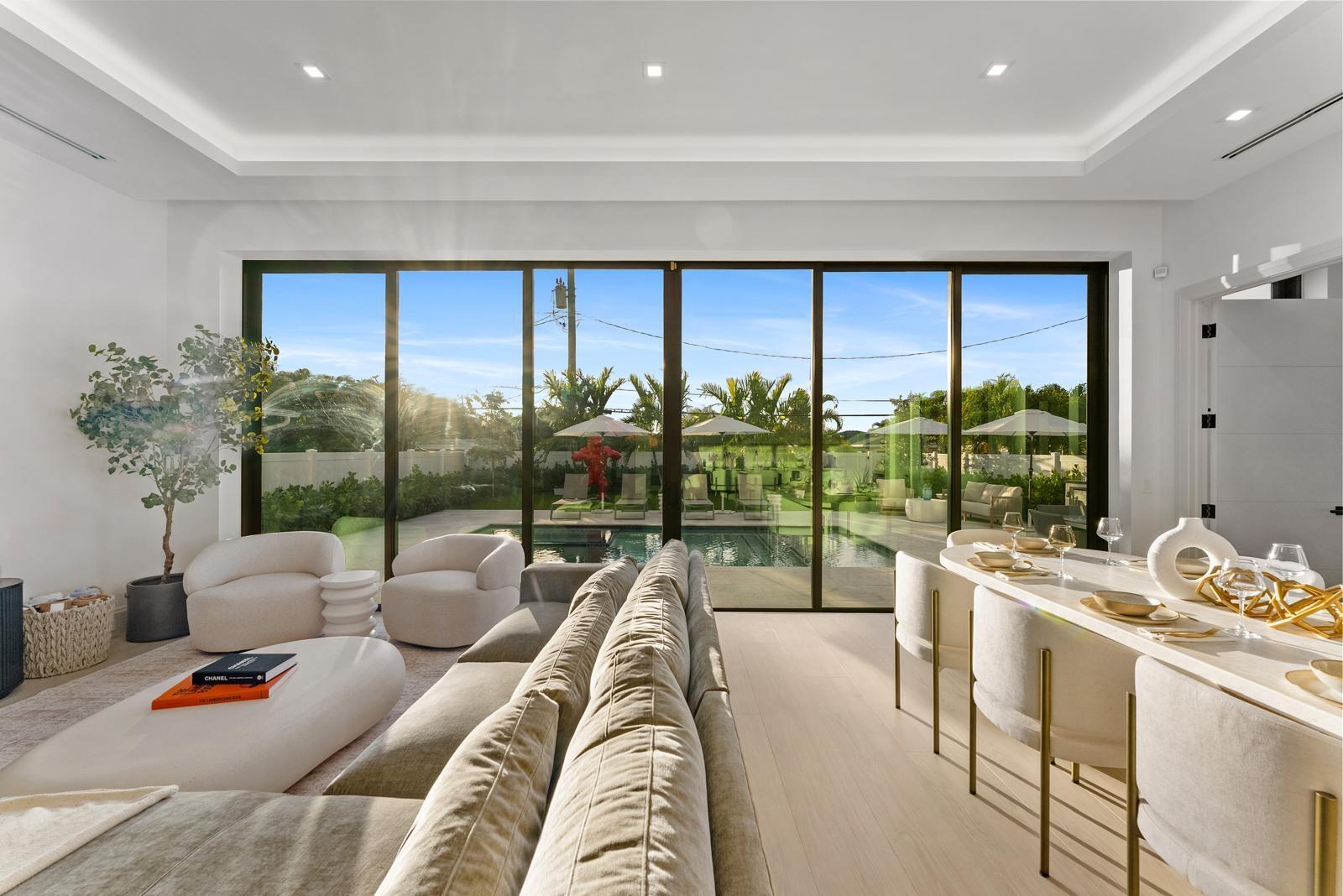 A modern living and dining area features floor-to-ceiling glass doors overlooking a backyard swimming pool — 220 S Swinton Avenue, Delray Beach FL 33444, DELRAY BEACH, FL