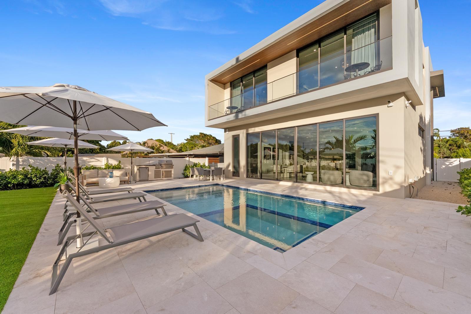 A modern two-story house features a swimming pool, lounge chairs, and an outdoor kitchen area — 220 S Swinton Avenue, Delray Beach FL 33444, DELRAY BEACH, FL