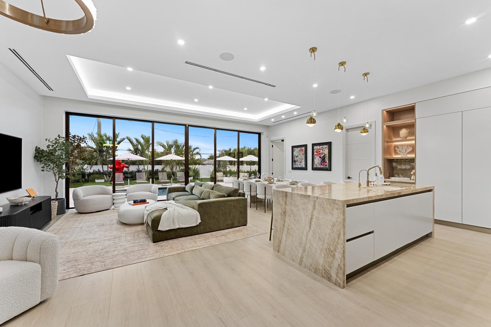 An open-concept living room and kitchen featuring a stone island, green sofa, and floor-to-ceiling windows — 220 S Swinton Avenue, Delray Beach FL 33444, DELRAY BEACH, FL