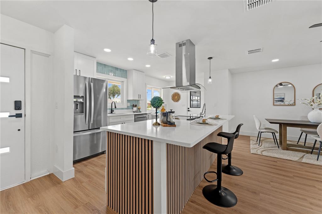 A modern kitchen features a slatted wood island, white countertops, stainless steel appliances, and flooring — 1406 SETON HALL DRIVE, SUN CITY CENTER, FL
