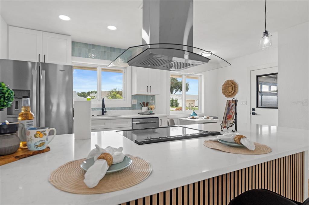 A modern kitchen features white cabinetry, a large island with a cooktop, and stainless appliances — 1406 SETON HALL DRIVE, SUN CITY CENTER, FL