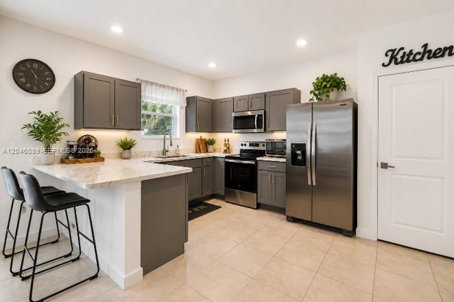 A kitchen features gray cabinets, stainless steel appliances, a breakfast bar, and tile flooring — 1707 SE 9th Ter, Homestead FL 33034, HOMESTEAD, FL