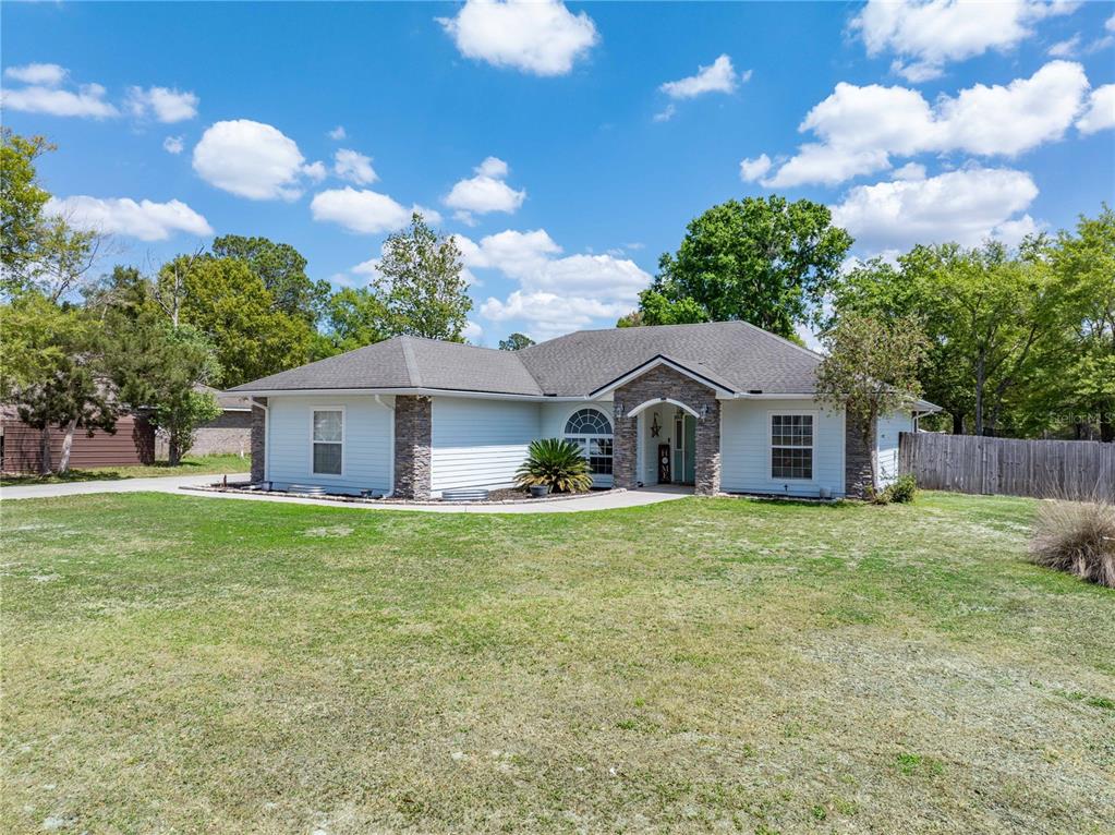 A single-story house with light siding, stone accents, and a covered entryway under a blue sky — 9312 SW 152ND COURT, LAKE BUTLER, FL