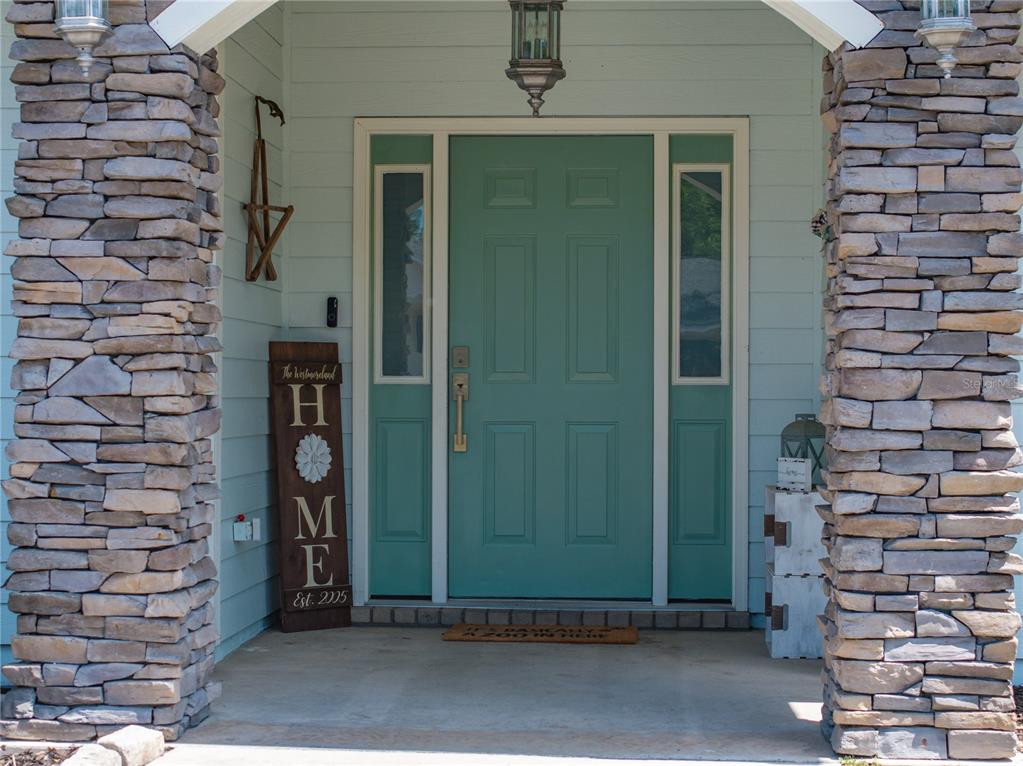 A teal front door is flanked by stone pillars and a wooden home sign — 9312 SW 152ND COURT, LAKE BUTLER, FL