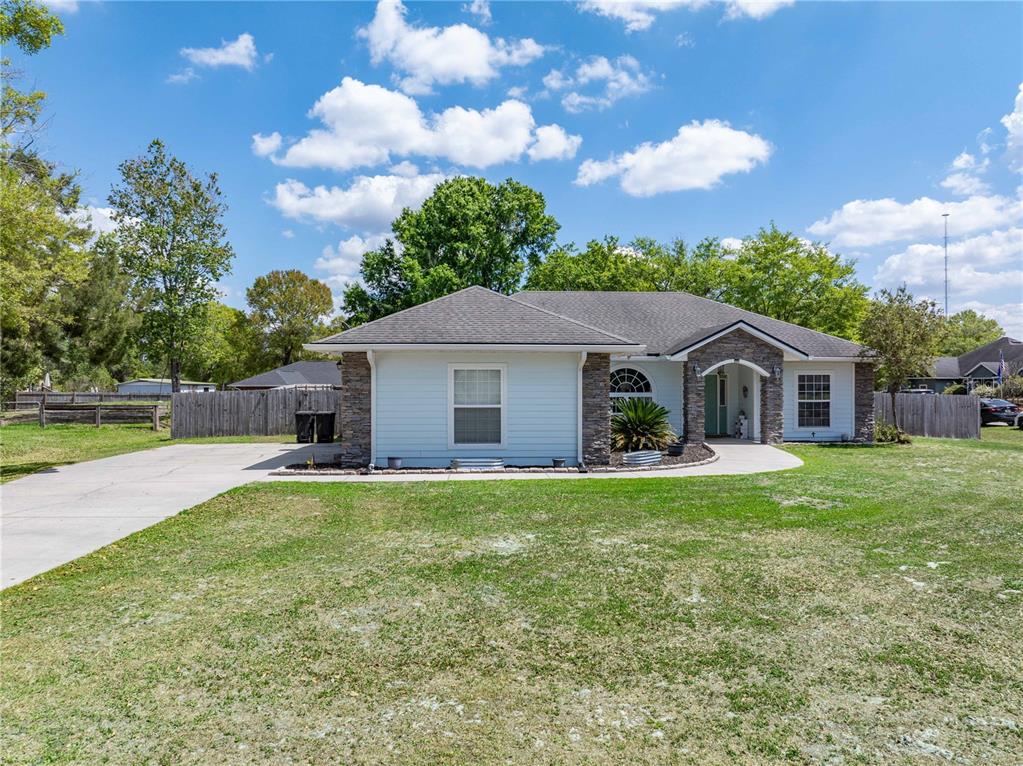 A single-story house with light siding, stone accents, and a concrete driveway under a blue sky — 9312 SW 152ND COURT, LAKE BUTLER, FL