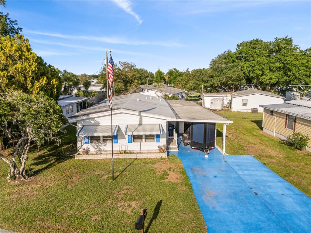 A white manufactured home features a blue driveway, a carport, and an American flag pole — 6034 ALPINE DRIVE, ZEPHYRHILLS, FL